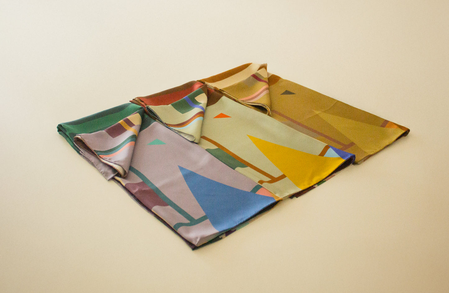 Triptych of folded silk scarves with geometric patterns on a beige background