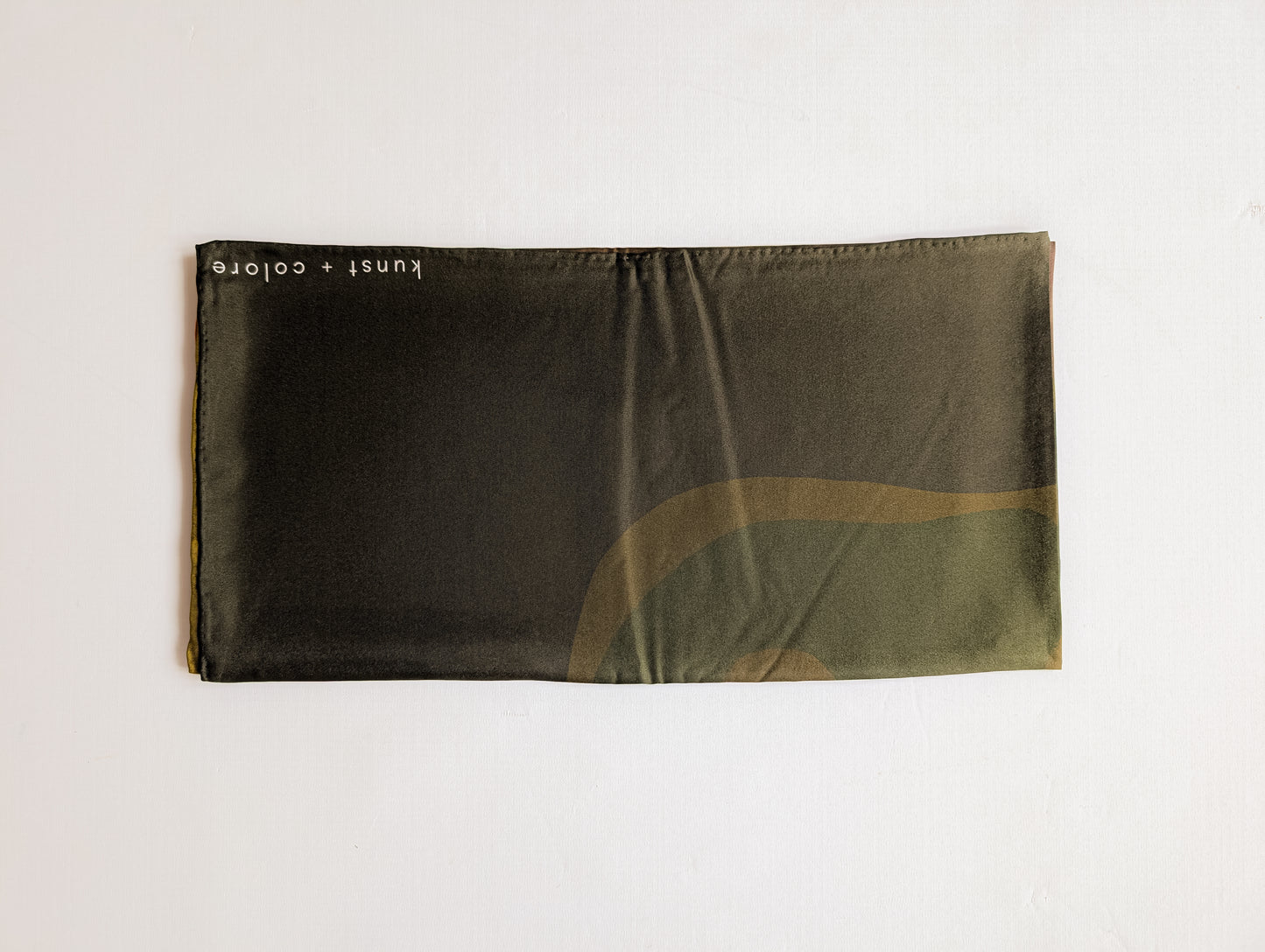 Green abstract print silk scarf folded on a white background