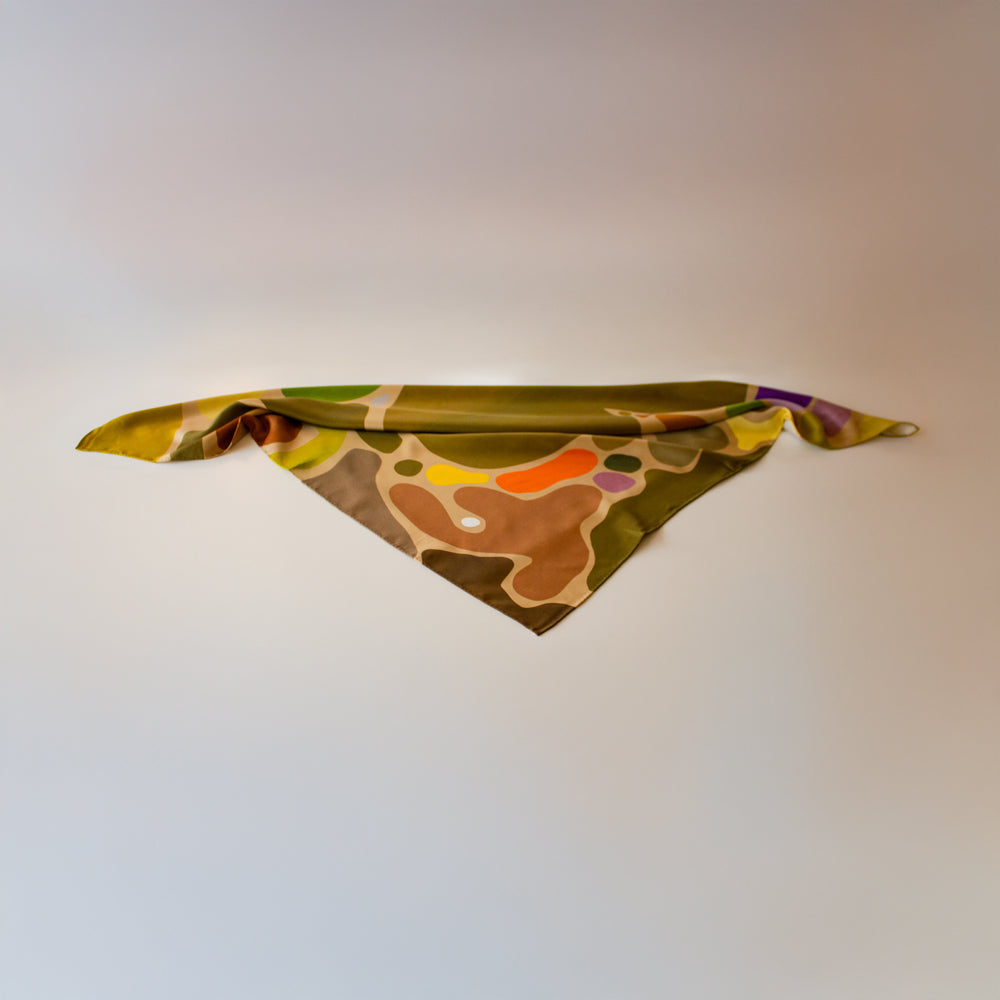 Eat Your Greens Silk Scarf by Kunst & Colore, featuring organic forms coloured in natural tones and bright pops of colour on an oaty beige background.  The scarf is folded on a white background arranged as though it were a neck tie. 