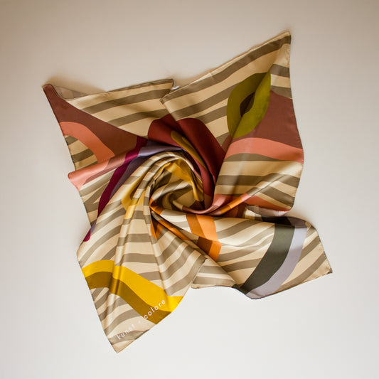 Taupe Tango by Kunst & Colore Silk Scarf, arranged artfully on a plain background.  The print of the scarf features undulating beige stripes on a beige background, with berry and natural hued organic shapes.