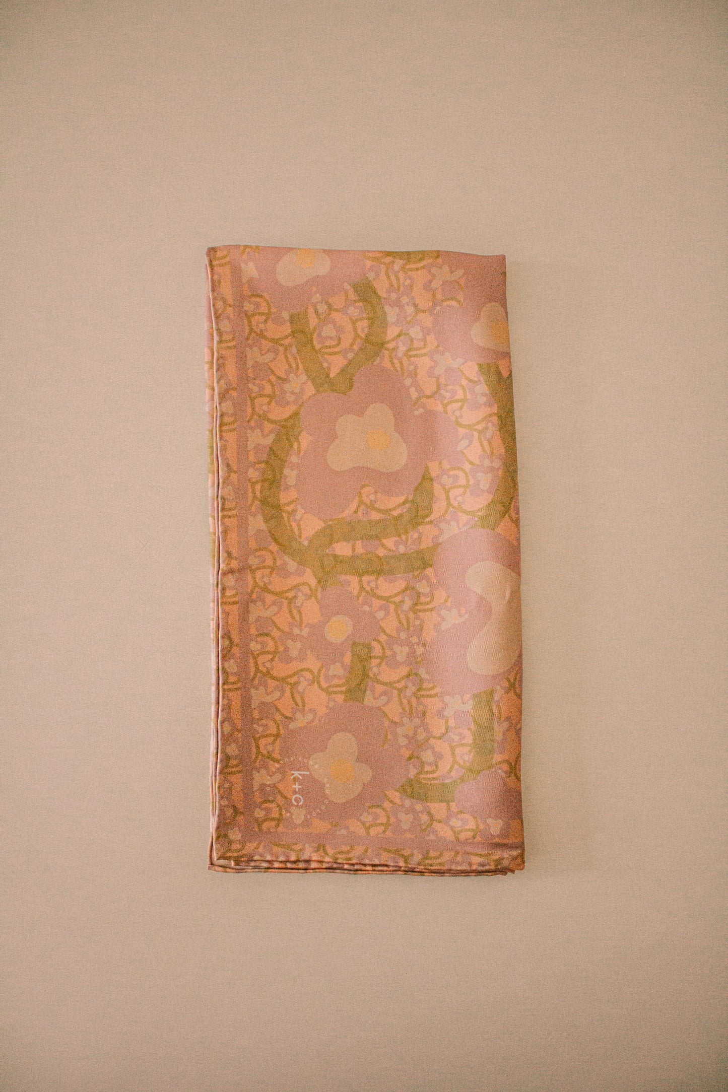 Patterned silk scarf with floral design folded neatly on a beige background