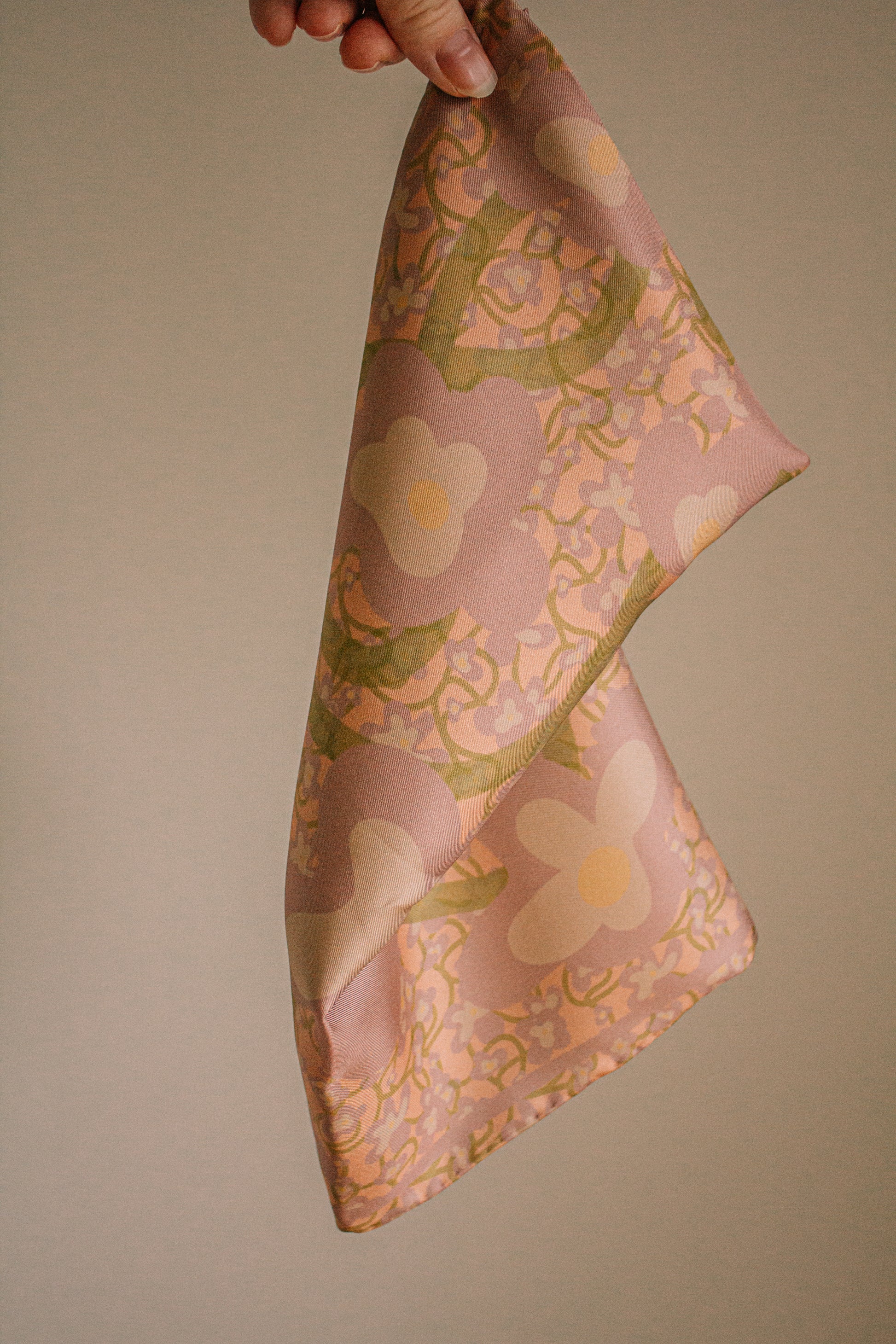 Floral patterned silk scarf held by a hand against a beige background
