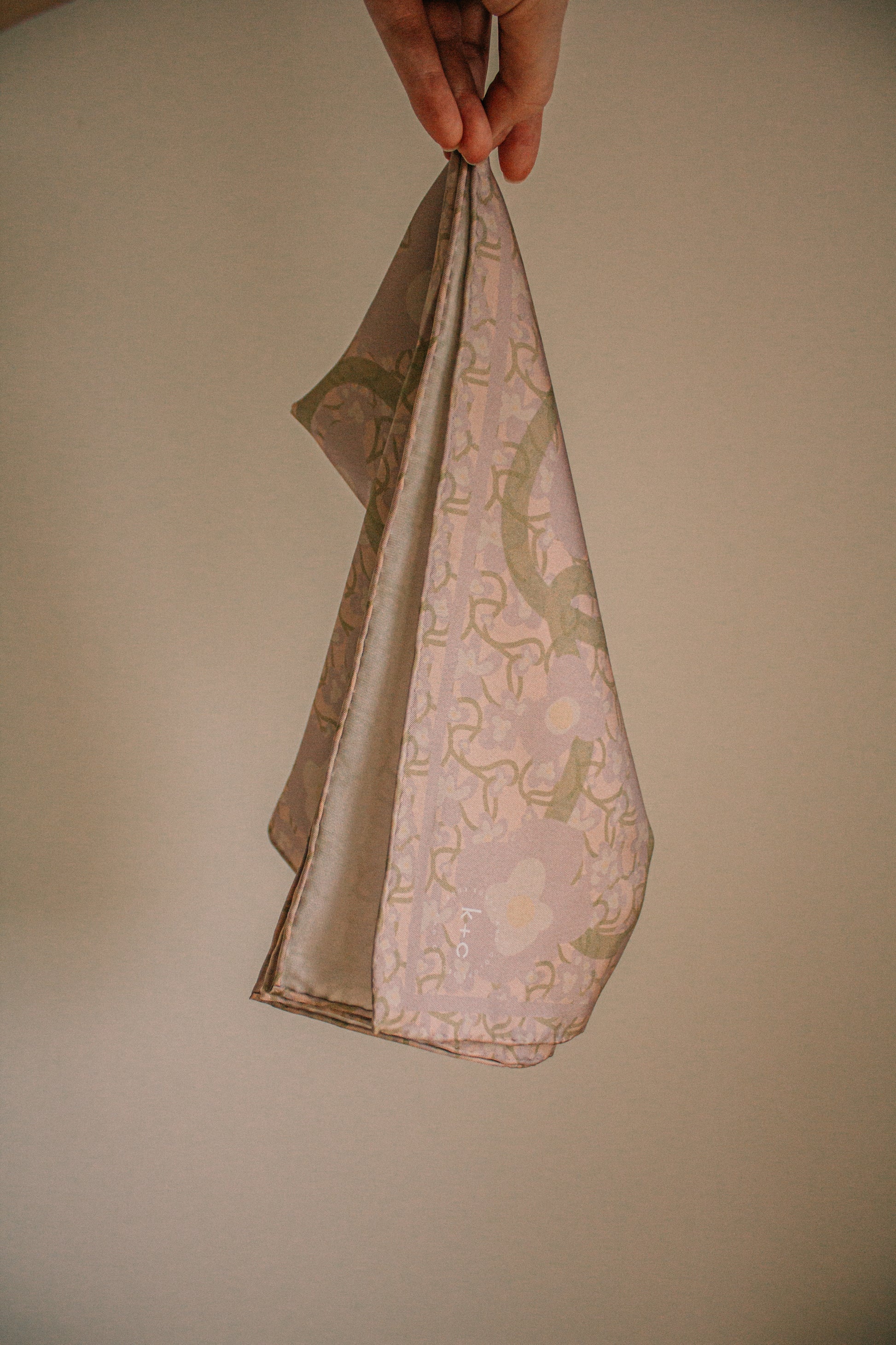 Hand holding a folded silk scarf with floral pattern against a plain background