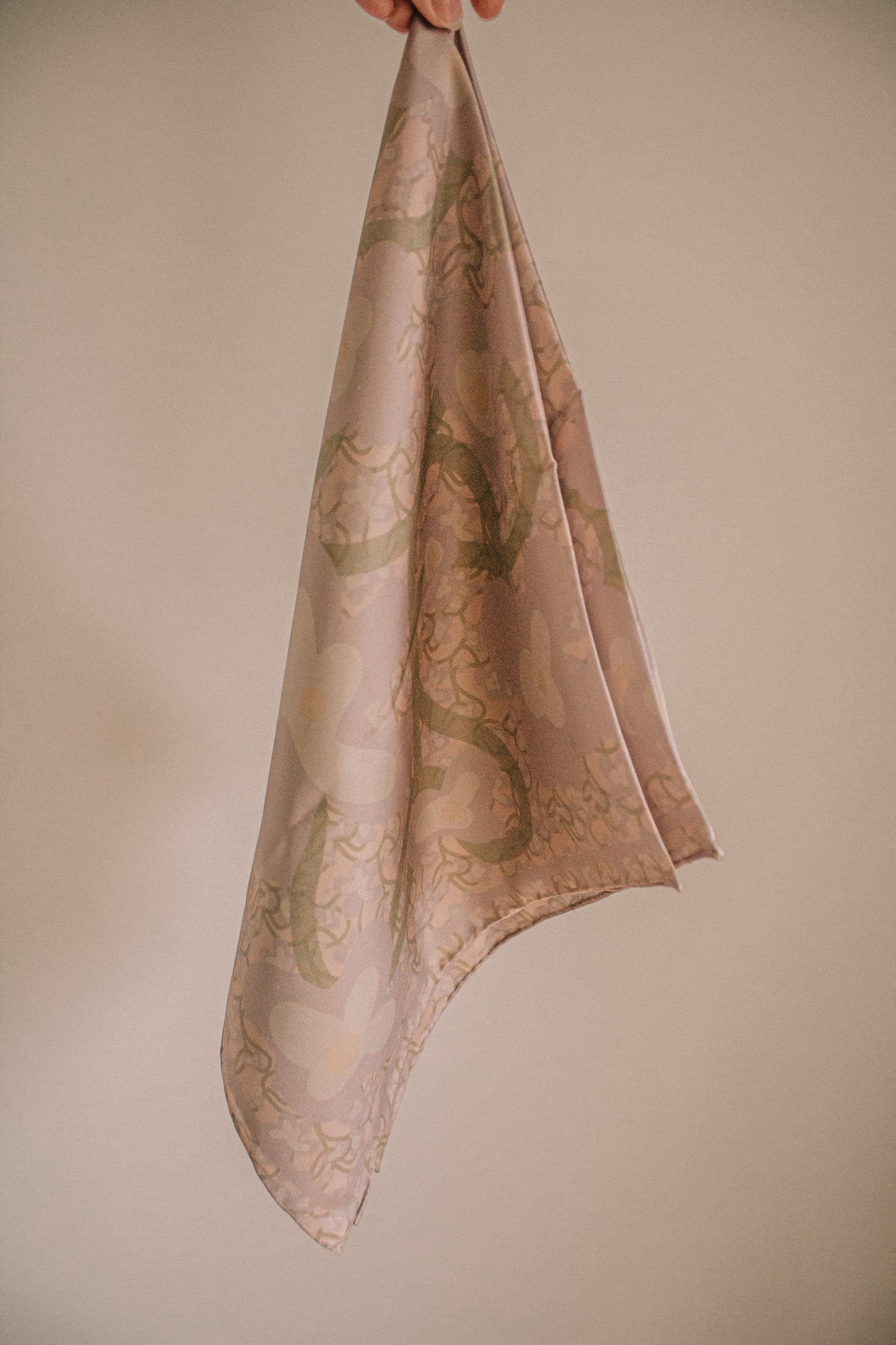 Silk scarf with intricate floral patterns held against a beige background