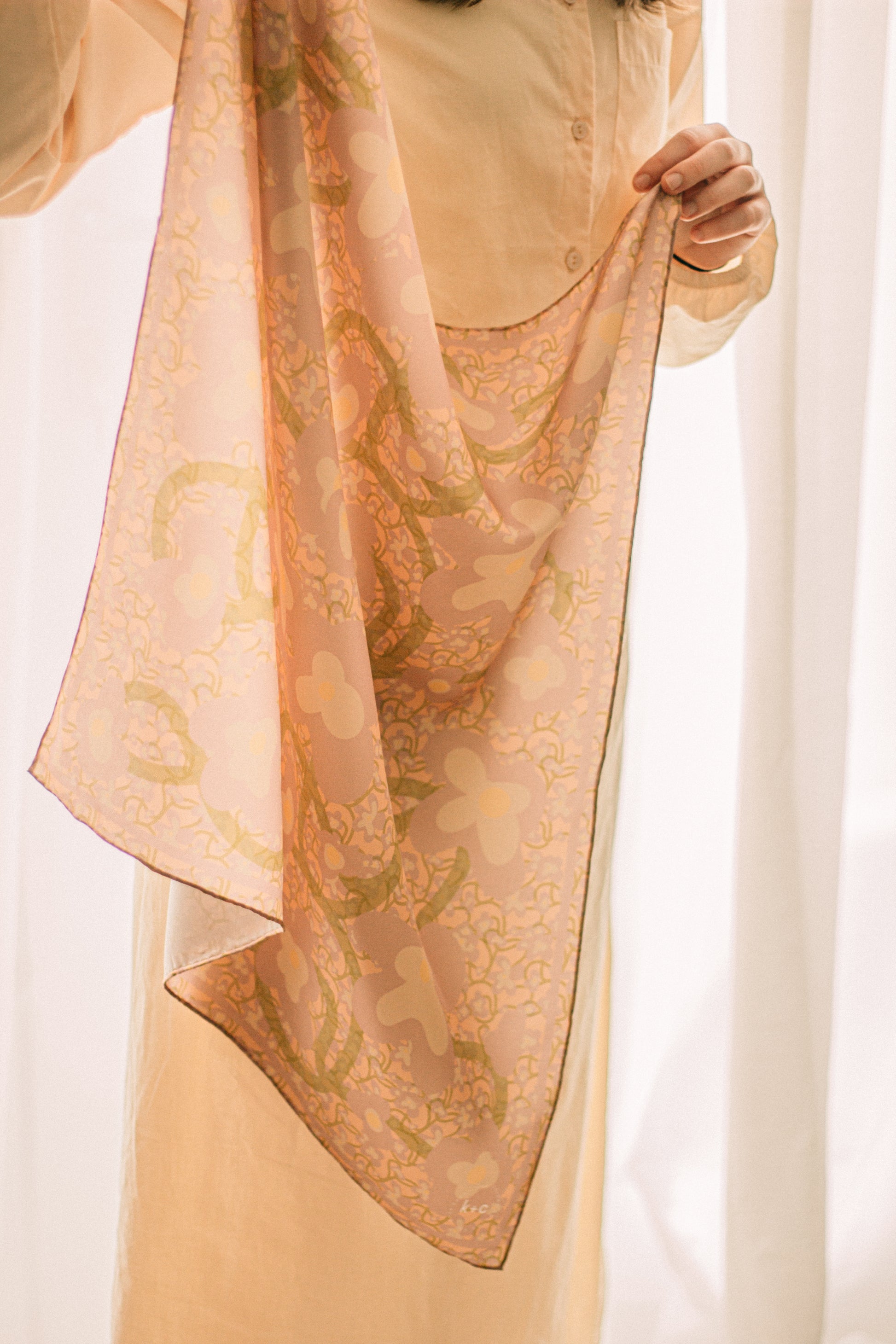 Person holding a patterned silk scarf with floral pattern against a sheer white backdrop