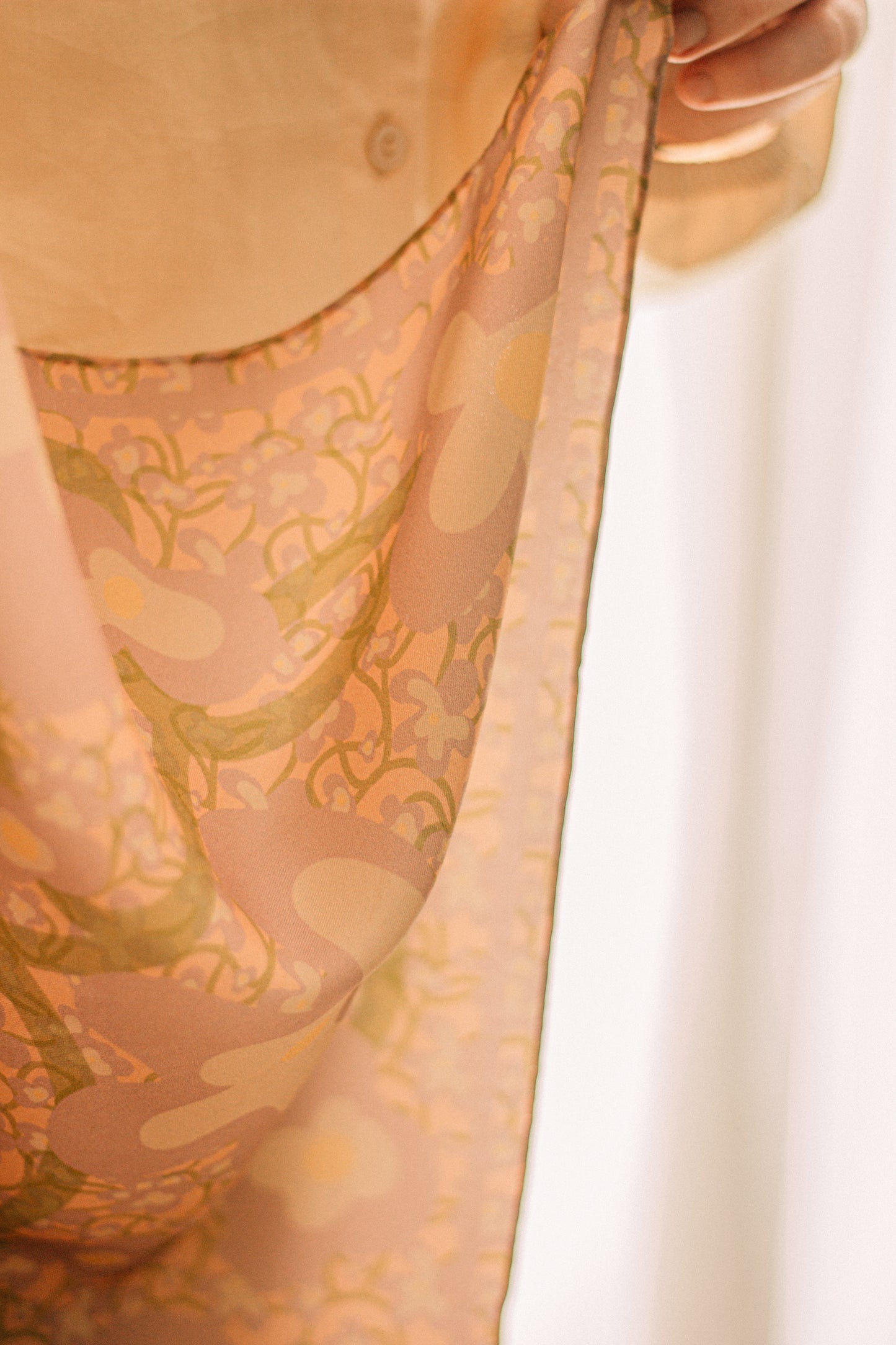 Close-up of a person holding a patterned silk scarf with floral pattern against a sheer white backdrop