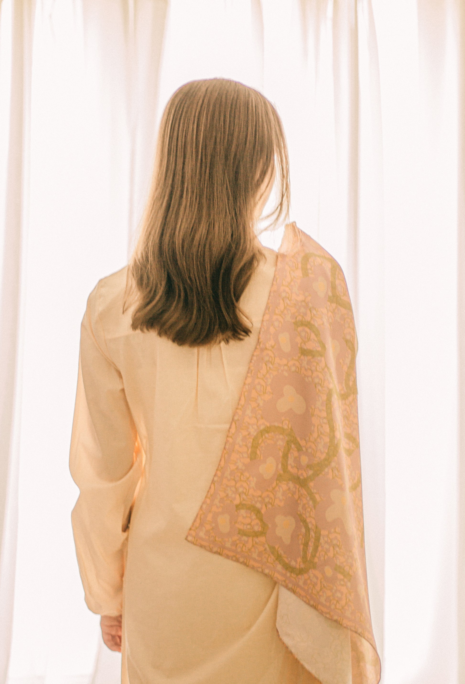 Woman wearing a patterned silk scarf with floral design over her shoulder against a white curtain background