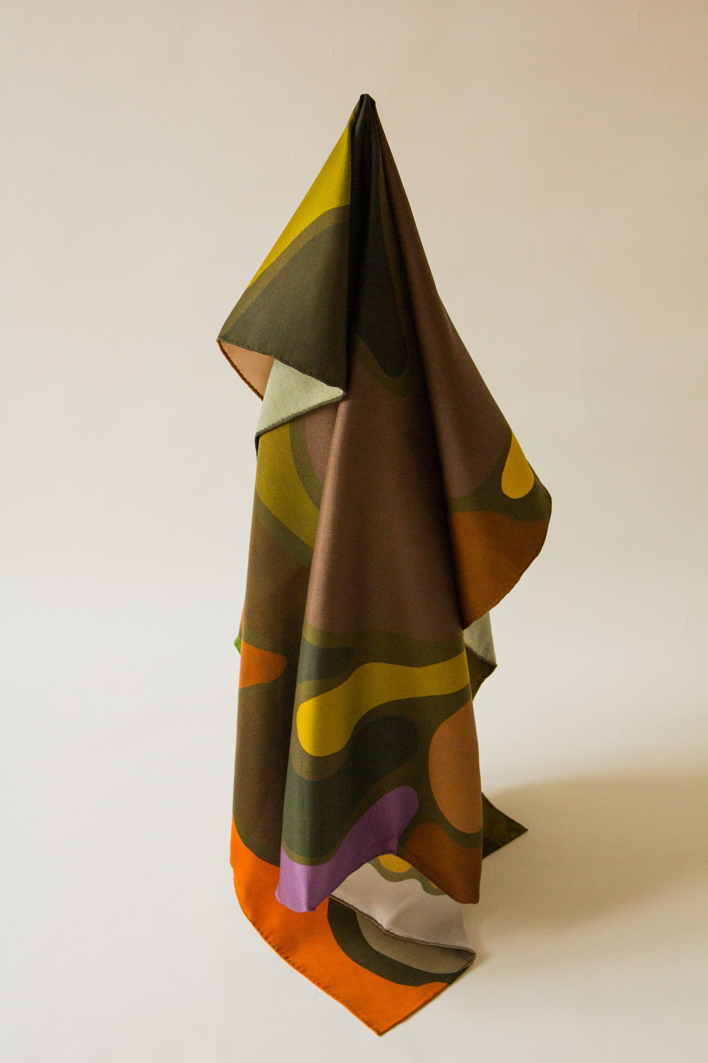 Olaf & Olive Silk Scarf by Kunst & Colore shown hanging artfully on a plain background.  The print features colourful pops of earthy tones on a khaki green background.