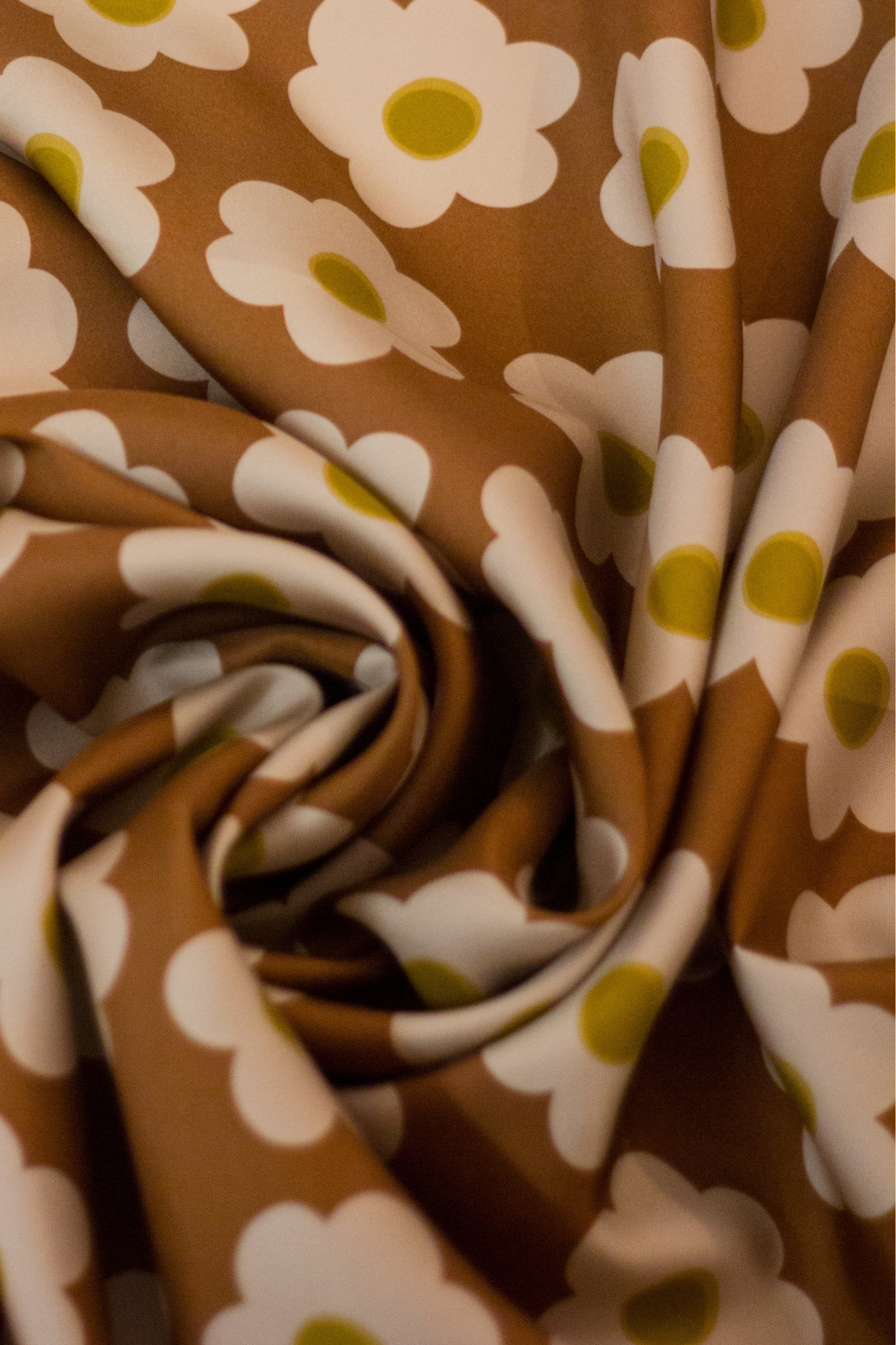 Detailed view of the 'Daisy Brown' scarf by Kunst & Colore. The print features small cream-coloured daisies arranged in a uniform square, on a brown background. 