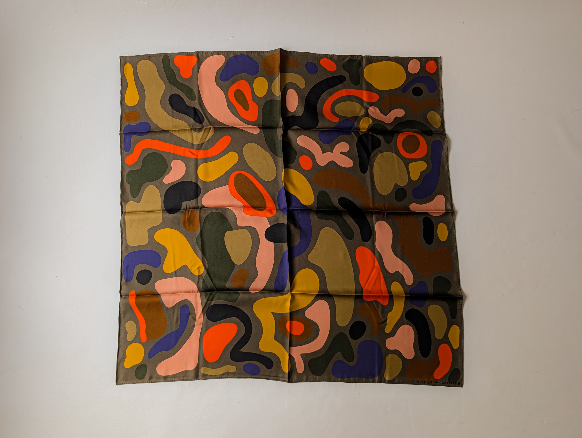 Abstract silk scarf printed with colorful organic shapes photographed on a plain background
